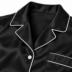 Close-up of ivory piping along the black silk nightshirt's collar and button placket.